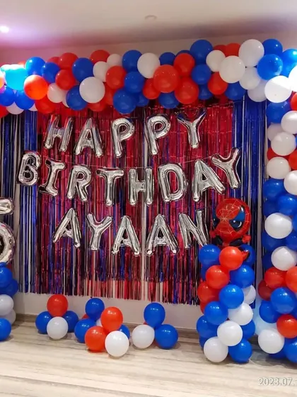 A Spiderman-themed 5th birthday party at home. The decor includes a red and blue balloon frame and a shimmer curtain backdrop.
