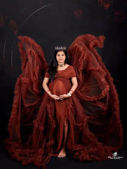 For a truly dramatic and powerful statement, we style portraits with our unique angel-wing gowns. This mom-to-be looks absolutely regal, framed by the flowing fabric against a dark, moody backdrop.