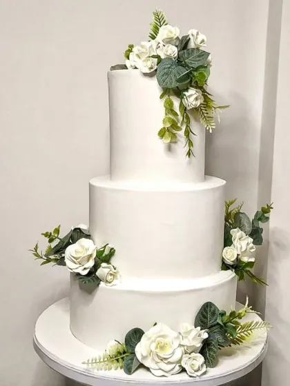 A classic and clean three-tiered white wedding cake. This design is all about understated elegance, adorned with arrangements of handcrafted white sugar roses and fresh-looking greenery. It’s a timeless choice that never goes out of style.