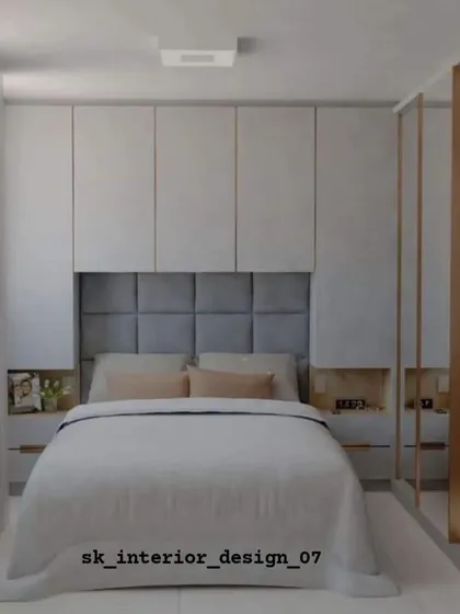 A cozy bedroom with a grey tufted headboard and integrated side niches. The mirrored wardrobe doors help to make the room feel larger and brighter.
