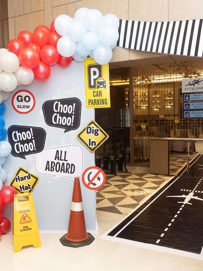 The entrance to the travel-themed party, designed to look like a roadway leading to an airport. The 'All Aboard' and 'Choo Choo!' signs set the tone for a journey of fun.