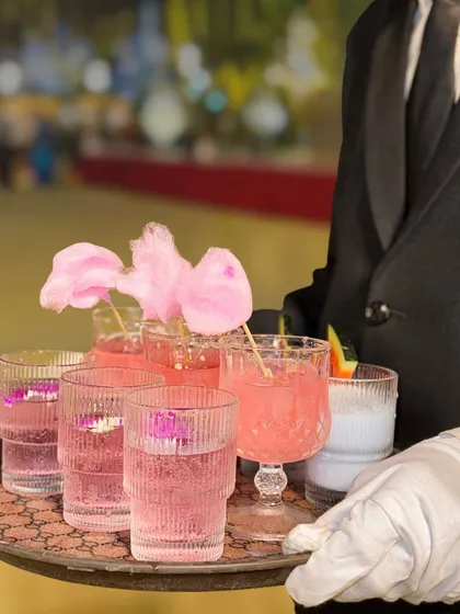 A server in elegant attire holds a tray of my signature mocktails. This image showcases the professional service and beautiful presentation of my beverage offerings, including the popular Pink Bubblegum drink.