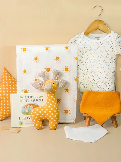 A sunny, yellow-themed baby hamper with a giraffe toy and sun-print blanket. The cheerful styling makes it a perfect gift for a summer baby.