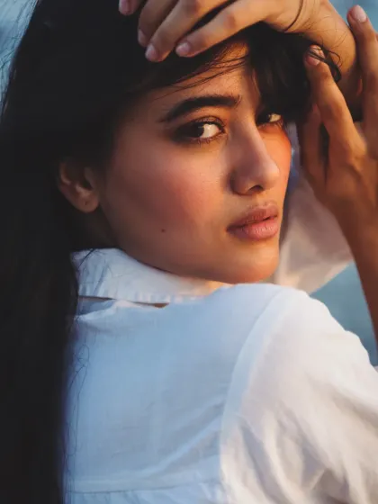 A golden hour beach portrait. The warm, direct sunlight creates a beautiful glow on the skin and an intense, captivating gaze.