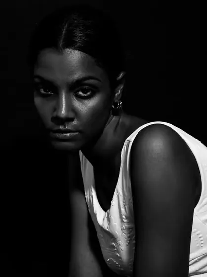 A high-contrast black and white portrait with an intense, direct gaze. The deep shadows create a dramatic and mysterious feel.
