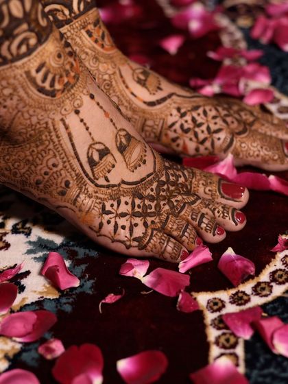 A close-up of a bride's feet, adorned with beautiful mehandi featuring jhumka (earring) motifs and surrounded by rose petals.