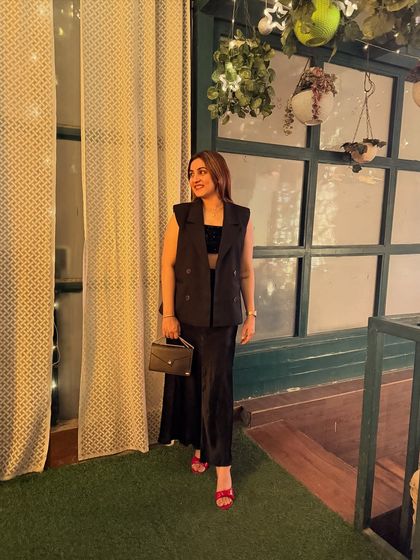 Command the room with structure, own the moment with flow. This all-black look, featuring a sleeveless waistcoat over a crop top and satin skirt, is all about bold, confident style. The pop of red from the heels adds the perfect finishing touch.