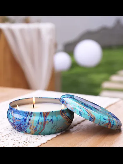 A lit tin candle with a beautiful marbled design, perfect for adding a pop of color and fragrance to any tabletop or outdoor patio setting.