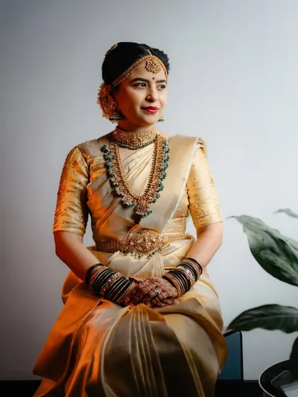 A seated portrait of the bride in the gold saree, her makeup glowing under the lights.