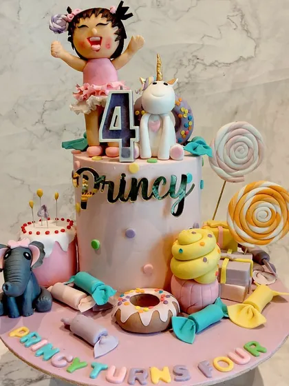 A whimsical cake for a 4th birthday, featuring a cute girl figurine, a unicorn, an elephant, and lots of candy-themed decorations like lollipops and donuts.