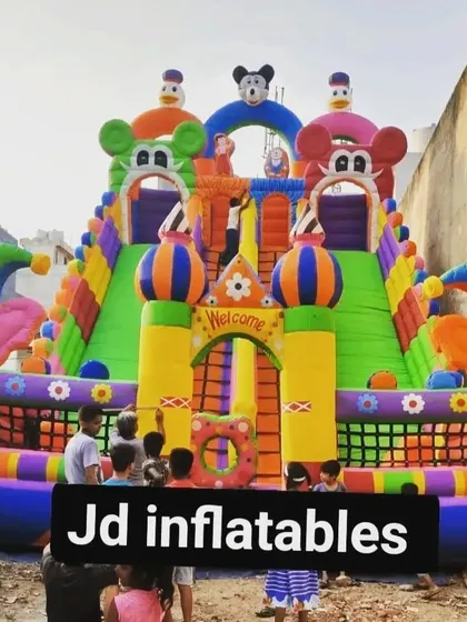 A large, colorful sliding bouncy with clown and Mickey themes, shown here being enjoyed by kids at an event.