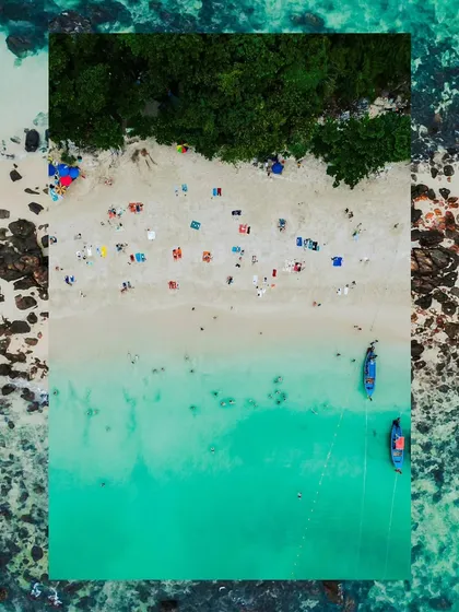 A creative, top-down drone shot of a beach in Thailand, framed to create an artistic composition. This view highlights the patterns of people, umbrellas, and boats against the sand and sea.