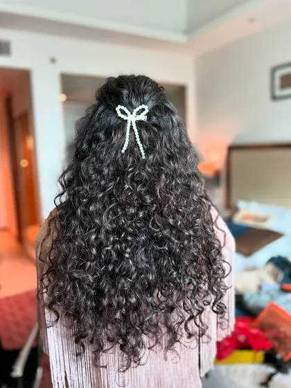 I absolutely love working with natural curls. Instead of straightening them, I focus on defining and celebrating your hair's texture. This simple half-up style with a handmade pearl bow lets the curls be the star of the show.