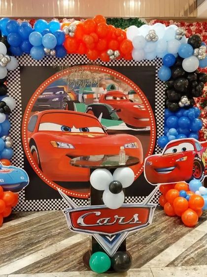 A vibrant Disney 'Cars' themed birthday stage with a Lightning McQueen backdrop, character cutouts, and a balloon arch.