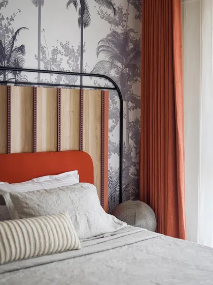 A detail shot of the custom tropical wallpaper and upholstered headboard in the master bedroom. The vibrant orange and natural wood tones bring a touch of the tropics indoors.
