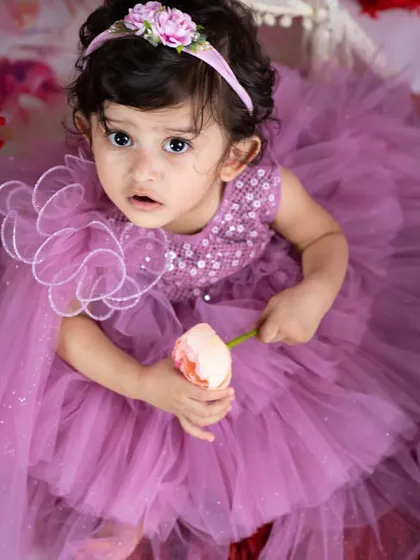 A beautiful portrait of a little girl in a lavender dress, holding a single flower. The soft, dreamy lighting enhances the fairy-tale feel.