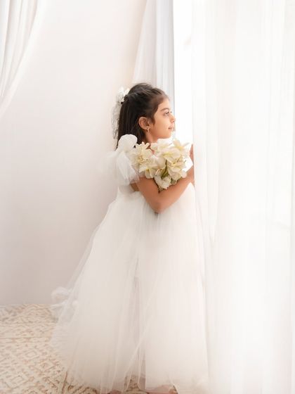 A pensive, beautiful portrait of a girl in a white dress, looking out the window as if lost in a daydream.