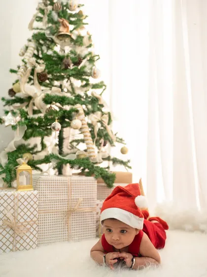Celebrate your baby's first Christmas with a festive photoshoot. This setup includes a decorated tree, presents, and a cute Santa hat for a perfect holiday card photo.
