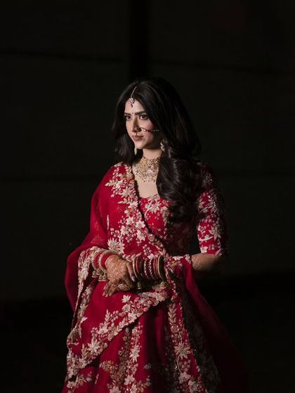 A classic portrait of the bride in her red lehenga. The dark background makes her and her intricate outfit stand out, creating a timeless image.