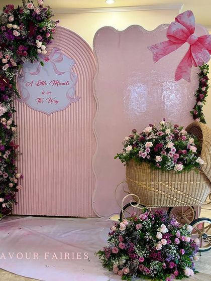 'A little miracle is on the way'. This elegant pink baby welcoming setup features a wicker baby bassinet filled with flowers, a large bow prop, and modern, textured backdrops.