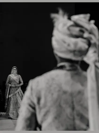 A powerful black and white shot of the groom's first look at his bride. The focus on her approaching figure from his perspective creates a moment of high anticipation and emotion.