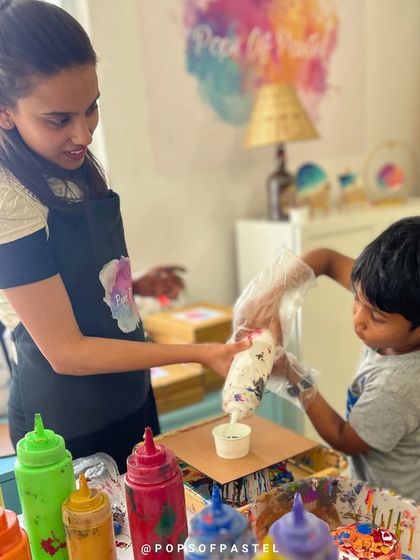 A young boy gets assistance in pouring his first colors, learning the basics of fluid art in a fun and supportive environment.