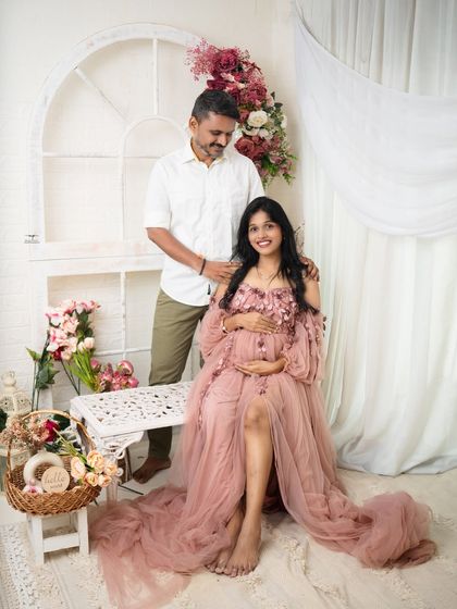 A full view of the family in a light-filled studio setting. The mother's flowing pink gown and the soft floral decor create a dreamy, romantic atmosphere.