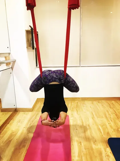 A student practices a supported headstand variation. The hammock takes the weight off the cervical spine, making it a much safer way to experience the benefits of this classic yoga pose.