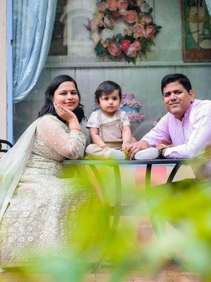 A charming family photo at our European-style cafe set. The pastel-colored wall, window, and outdoor table create a romantic and sweet setting for portraits.