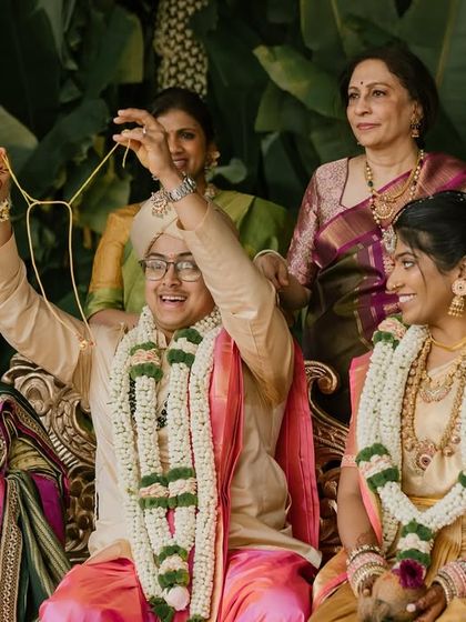 The groom joyfully displays the thali, a significant part of a South Indian wedding, with his bride and family beside him.