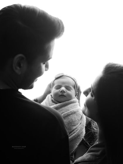 A classic black and white silhouette shot from a different angle, showing the parents looking down at their peacefully sleeping baby.