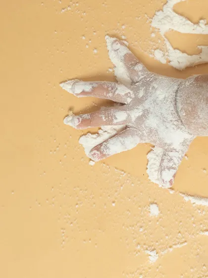 A close-up of a baby's handprint in flour. This artistic detail shot captures the sensory experience and messy fun of our 'Baby Chef' theme, preserving a tiny moment in time.