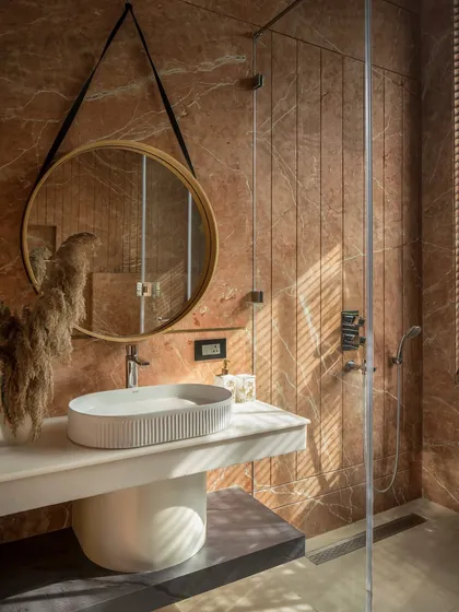 The success of a facade is felt within. In this bathroom at Twin Villa, the exterior screens filter the morning sun, casting gentle, linear shadows across the warm stone. This is how architecture becomes personal, shaping quiet moments and the sensory experience of a home.