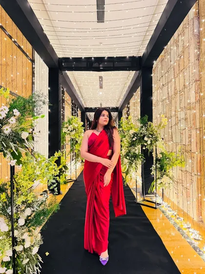 A full-length view of a beautiful red saree in a grand, lit-up corridor. The purple heels add a fun pop of color to the classic look.