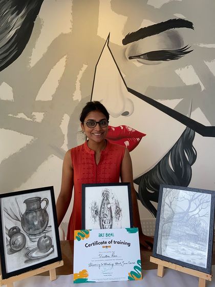 A proud student poses with her certificate and three detailed sketches. The studio's iconic mural makes for a great photo backdrop.