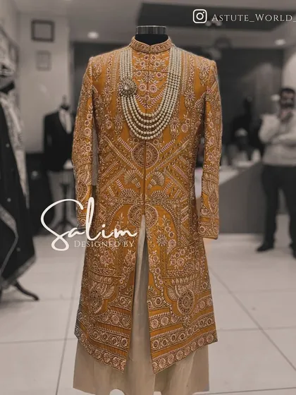 A sherwani displayed on a mannequin, showcasing the incredible density of the hand embroidery. This mustard-colored piece is a testament to the hours of craftsmanship that go into each wedding garment.