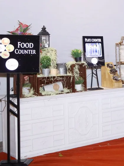A clearly marked and organized food counter at a formal event. The digital sign and rustic decor elements ensure a smooth and pleasant experience for all attendees.