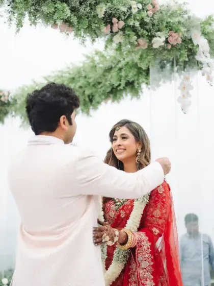 The groom places the garland around his bride's neck under a beautiful floral hoop. Her upward glance at him is a moment of pure adoration and connection.