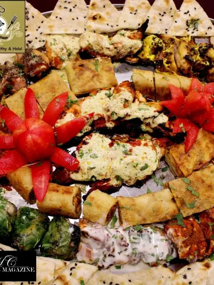 A beautifully arranged Mughlai thaal featuring a variety of kebabs, rolls, and creamy starters. The tomato carving in the center adds a touch of artistry to this abundant platter.