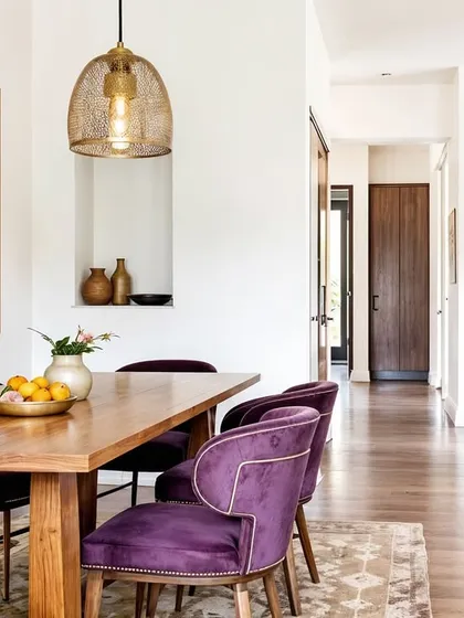 In this concept, plush purple velvet chairs add a pop of color and luxury to a rustic-modern dining space with warm wood and a traditional jali window.