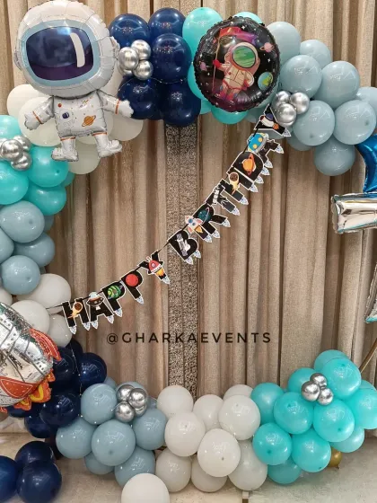 A simple and sweet astronaut-themed birthday decoration. This circular balloon arrangement in shades of blue and white is accented with rocket and astronaut foil balloons.