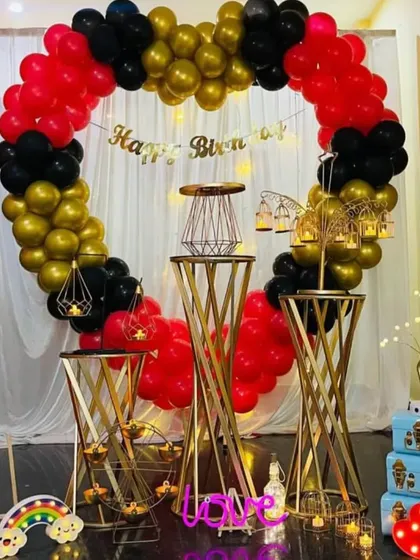 An elegant birthday surprise setup with a red, black, and gold balloon heart, and ornate gold pedestals.