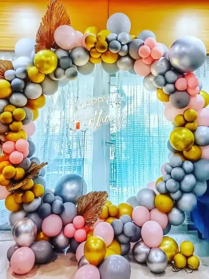 A trendy balloon ring decoration using a mix of pastel, metallic, and chrome balloons, accented with dried palm leaves for a bohemian touch.