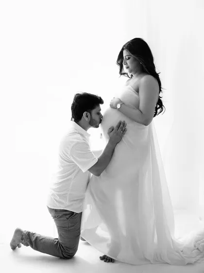 A classic pose of a partner kissing the baby bump, made even more poignant in black and white. It’s a timeless expression of love and anticipation.