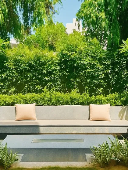A minimalist concrete fire pit and built-in seating area, surrounded by a dense wall of bamboo and other greenery. This creates a modern yet natural space for relaxation.