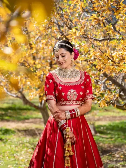 The bride in her stunning red lehenga, framed by the golden leaves of autumn in Sangla Valley. The vibrant colors of her attire against the fall foliage create a breathtaking contrast.
