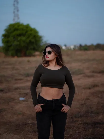 A portrait of a model in a crop top and jeans, set against a natural, outdoor background at dusk. The soft light and her confident pose create a beautiful and moody image.
