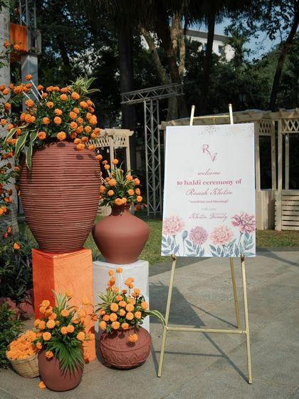 The welcome area for the Haldi, featuring a personalized sign and an artistic arrangement of marigolds in terracotta vases of various shapes and sizes.