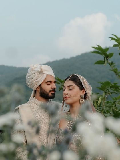 A close-up portrait of the couple amidst flowers, with the misty hills of Dehradun in the background. Their gentle expressions and the soft, natural light create a deeply romantic and serene image.