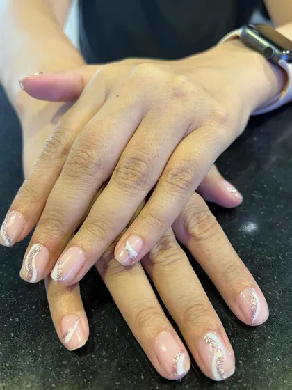 Subtle elegance on natural nails. This design features a sheer nude base with delicate white and silver glitter swirls, offering a sophisticated and minimalist nail art option.